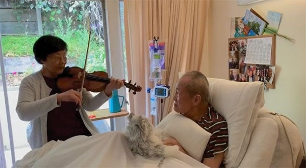 woman playing violin as man in hospital bed looks at her