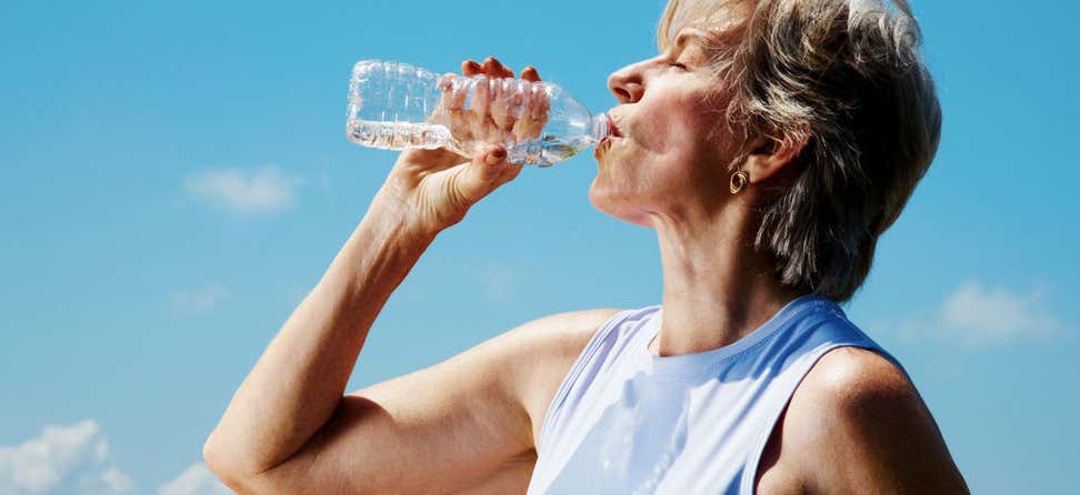 A senior Caucasian woman is drinking water from a water bottle outside.