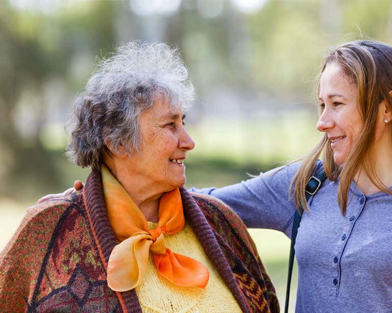 A senior woman is looking at her younger female caregiver lovingly outside.