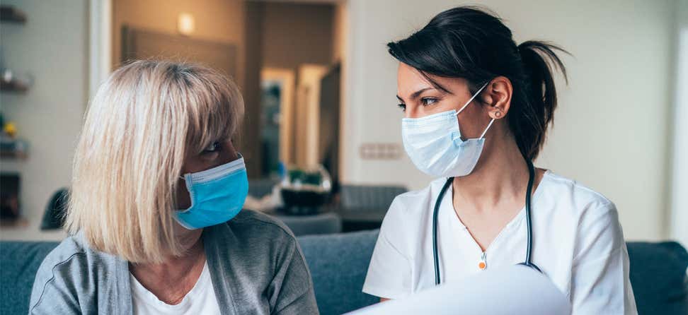 A doctor is consulting a senior woman about her medical condition, both wearing masks.
