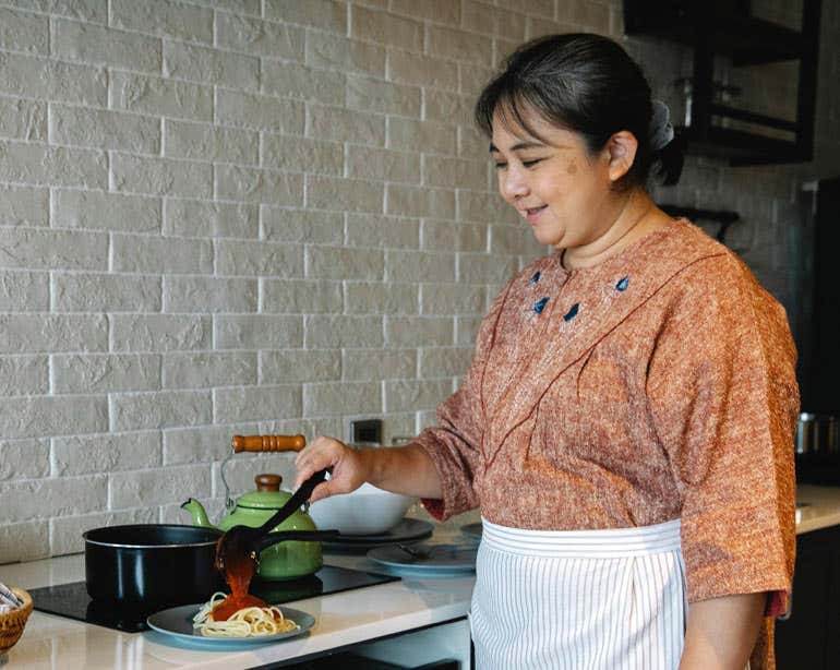 An older Asian senior woman is seen preparing food in her kitchen.