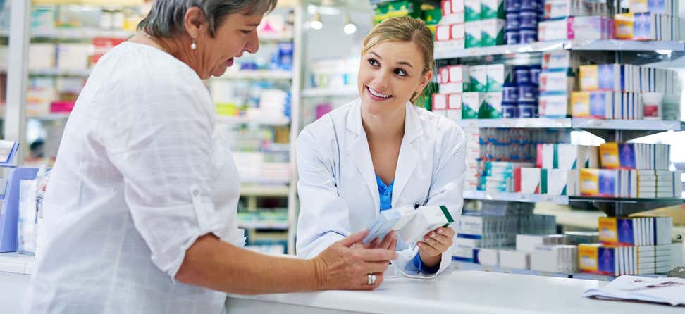 A young pharmacist behind the counter is giving prescription instructions to her senior female client.