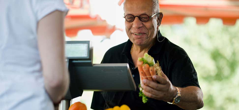 A Black man is checking out at an outdoor market, purchasing produce.