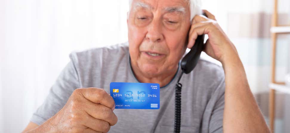 A senior man is on the phone, holding his credit card as if he's going to make a purchase.