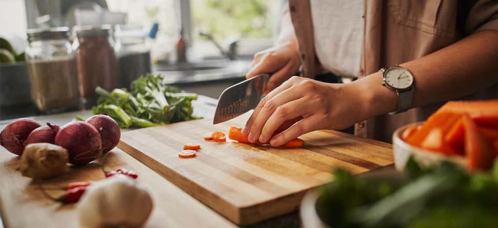 A woman off camera is slicing carrots in her kitchen, among other healthy vegetables.