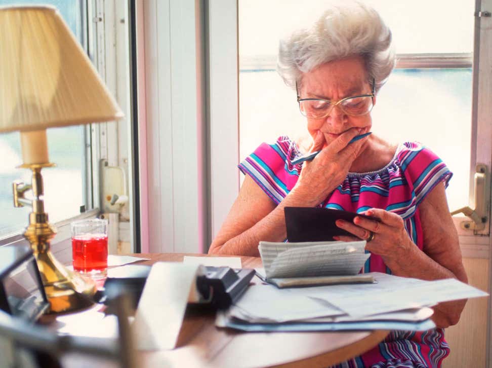 A senior Caucasian woman is balancing her checkbook at the kitchen table, thinking about retirement.