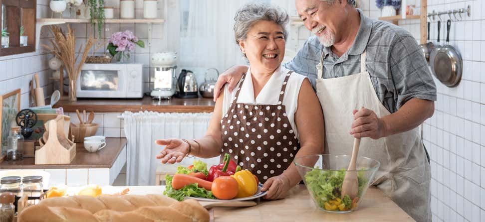 A senior Asian couple are embracing while preparing a healthy meal in their kitchen.