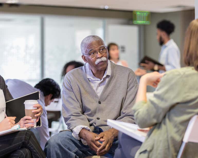 A Black senior man is sitting in a group having a discussion with other older adults.