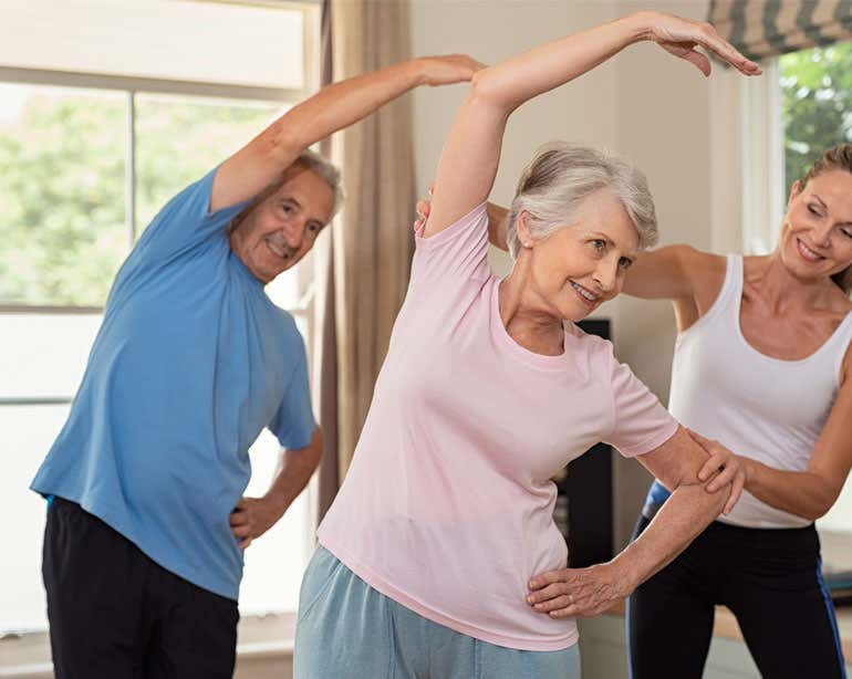 A young female trainer is helping a senior Caucasian couple with stretching exercises at home.