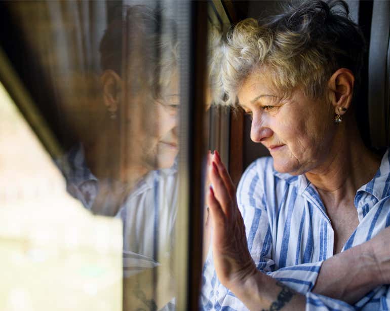 A sad, Caucasian senior woman stares out her window.