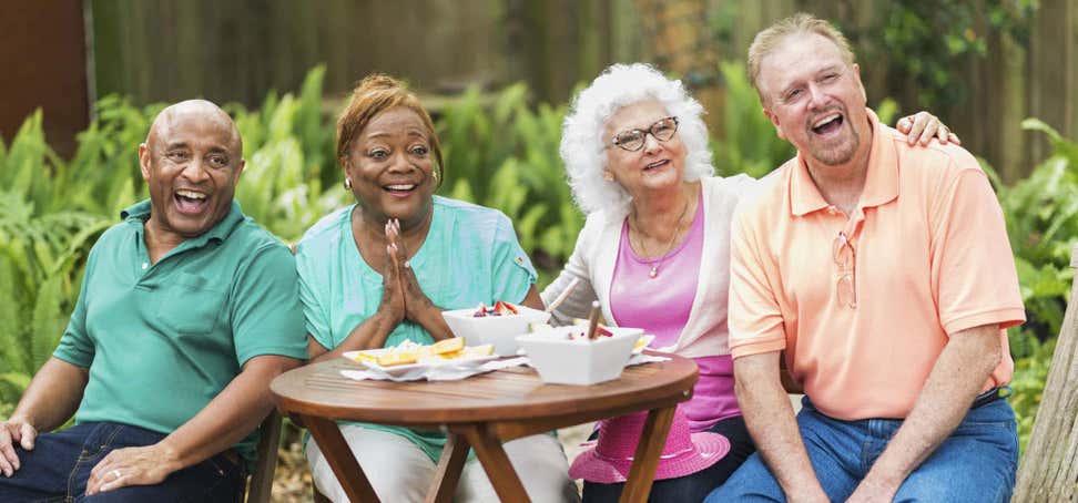 Two senior couples are outside enjoying a meal together, laughing and having a good time.