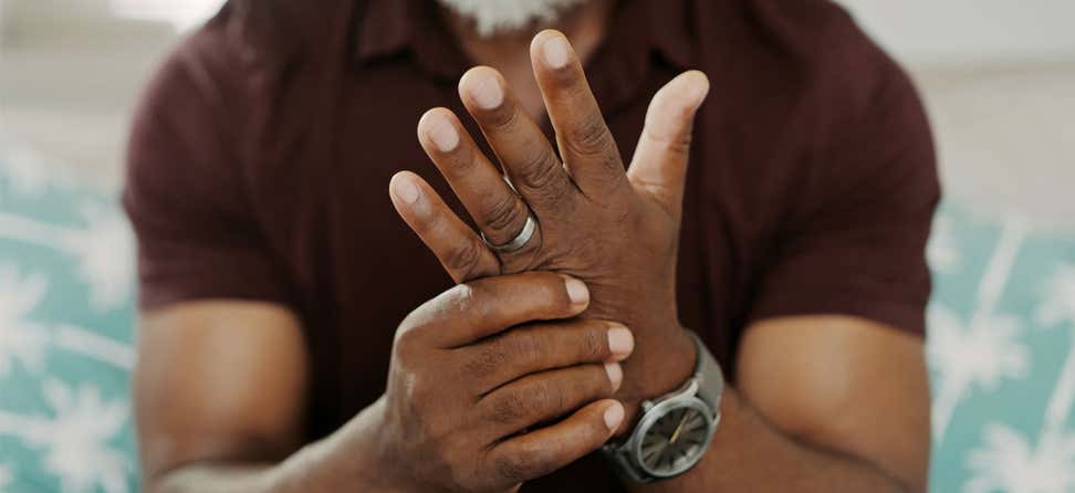 Cropped shot of a Black man sitting down, suffering from arthritis in his hand.