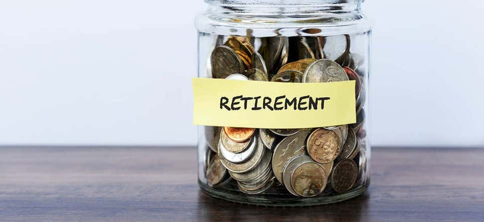 A jar filled with various coins has a sticky note with the words "Retirement" on it.