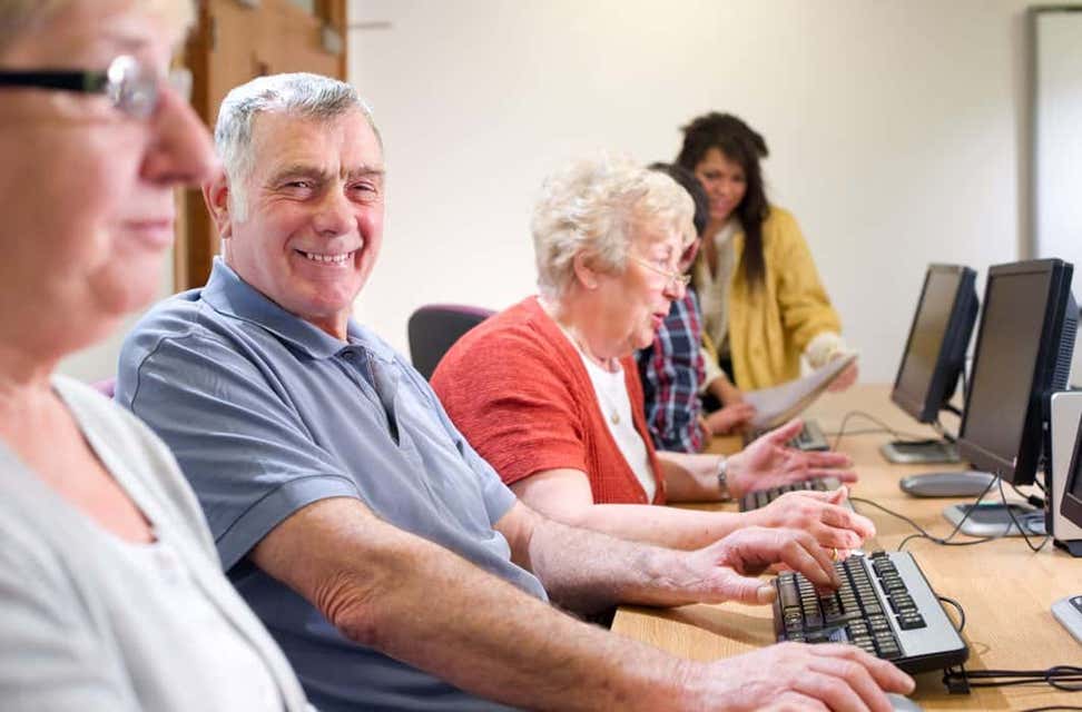 A group of seniors are smiling on a job training site while doing work on computers.