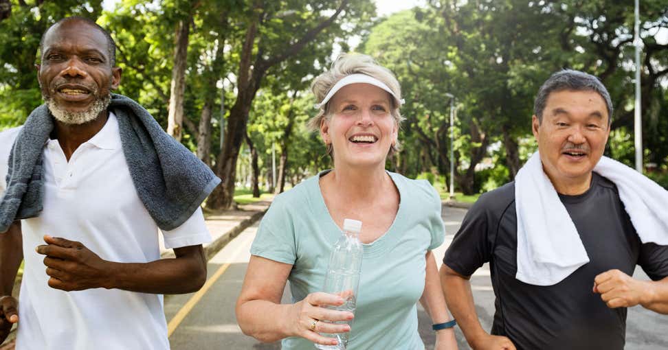 A group of older adults are running in the street for exercise, the senior woman carrying a water bottle.