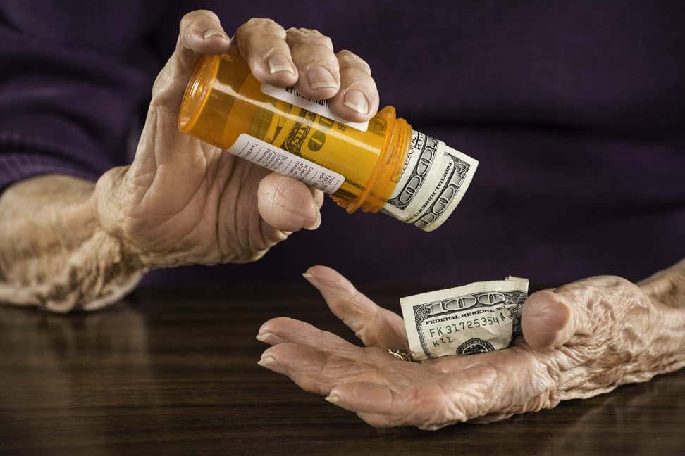 Older woman's hands shaking out $100 bills from prescription medicine bottle.