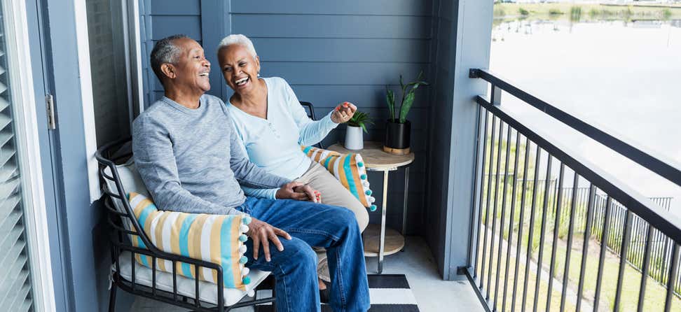 A senior Black couple is laughing and enjoying their time together on their porch.