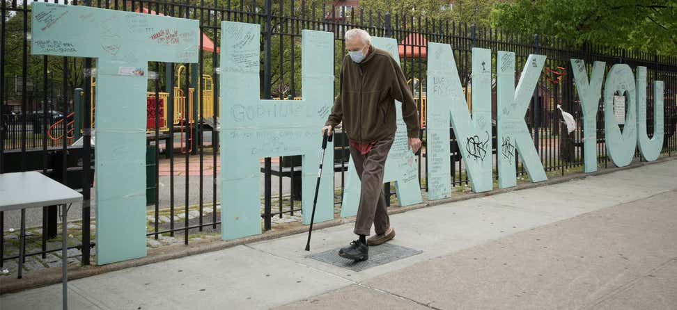 senior man wearing a face mask walks by a sign supporting health care workers
