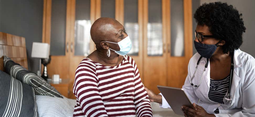 A Black senior woman wearing a mask is talking to her health care provider at home.