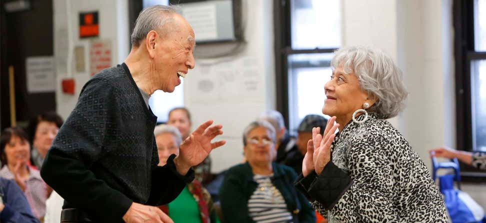 Two older adults are dancing together in front of a group at a local senior center.