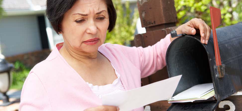 An older Asian woman checks her mail, staring with a confused look at a piece of mail she's picked up.