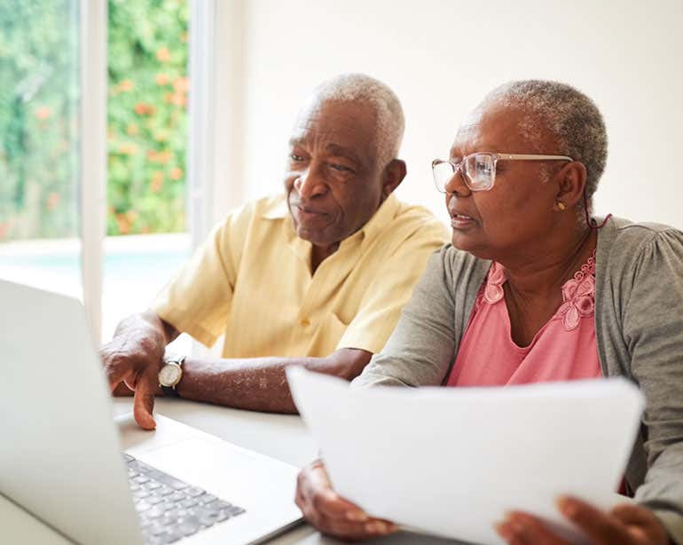 A senior Black couple are working on finances together while using a computer.