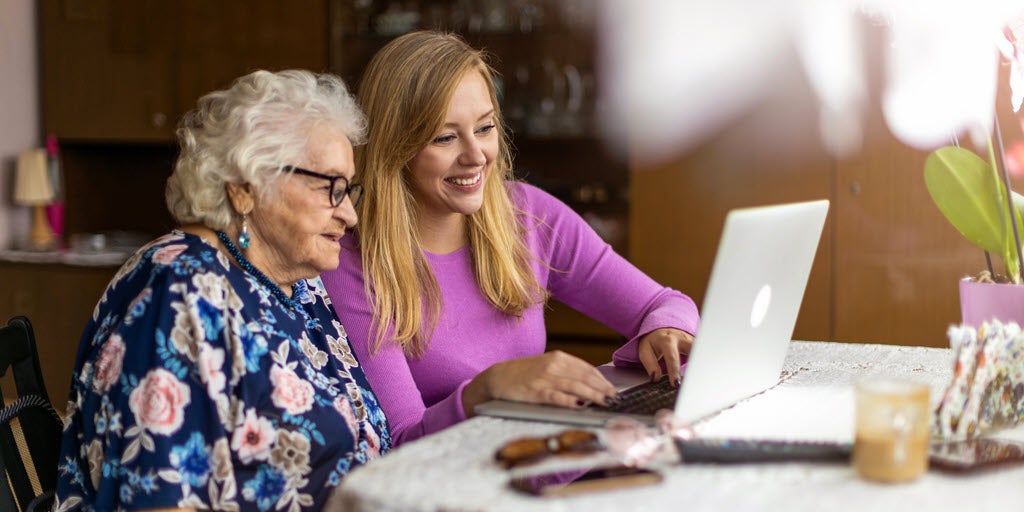 Younger woman helping older woman on laptop