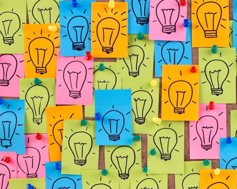 lightbulbs drawn on blue, yellow, and orange sticky notes pinned to bulletin board