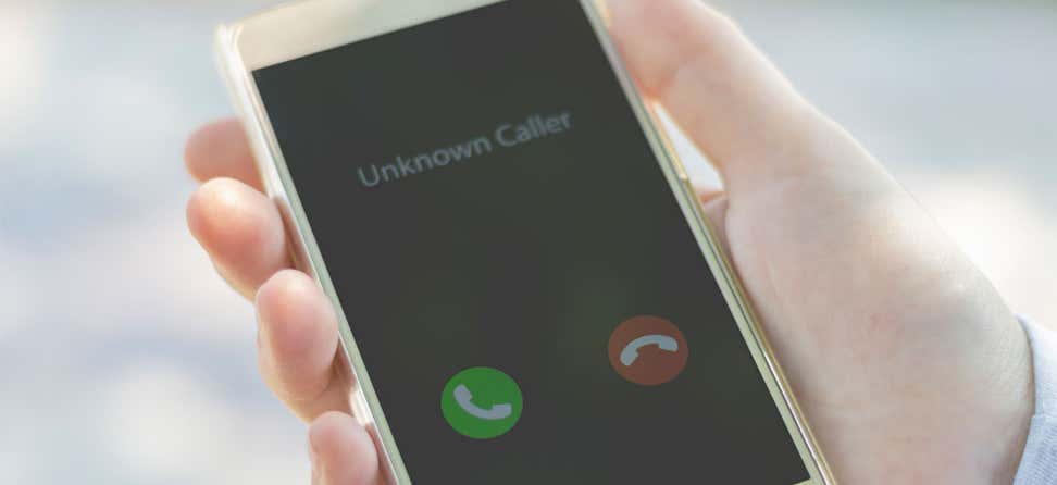 A man holds a cell phone in his hand that says "Unknown Caller", likely indicating a scam.