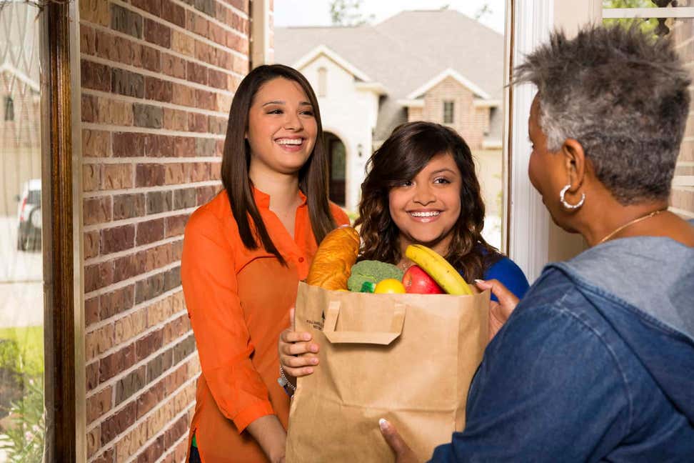 Two teenage girls delivering food bag to older black woman