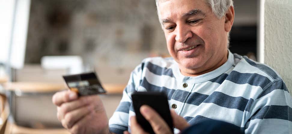 A senior Hispanic man is using his credit card while making an online purchase.