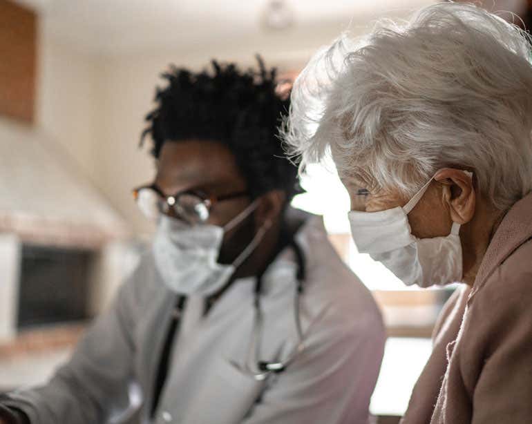 An older woman wearing a mask is having an in-person health care visit with a doctor during the pandemic.