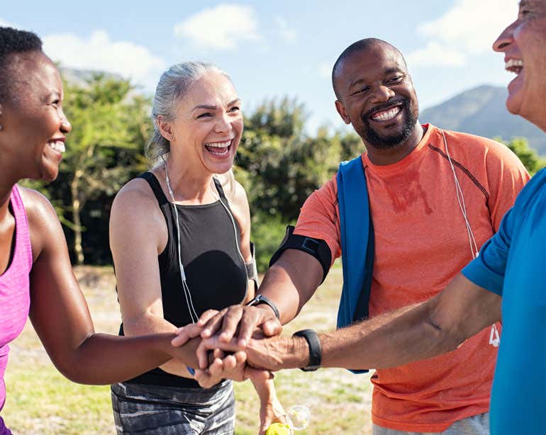 A group of diverse older adults put their hands in for a team high five while exercising outside.