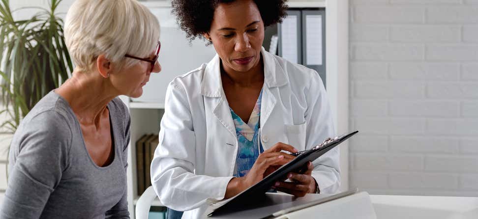 senior white woman confers with black female doctor with clipboard