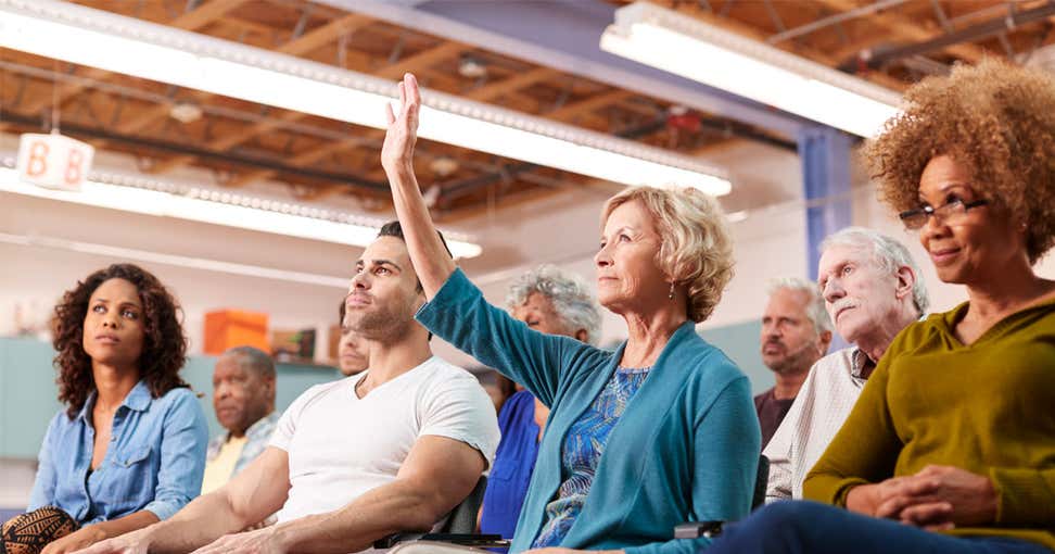 A woman raises her hand to ask at question at a community townhall with her member of Congress.