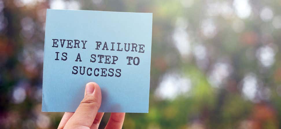 A close-up shot of an inspirational quote, "Every Failure Is A Step to Success" on a blue note card.
