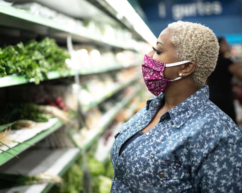 Older Black woman in produce section of grocery store, wearing face mask.