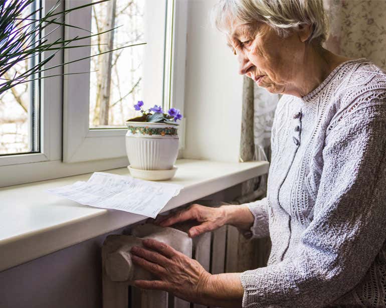 A senior Caucasian woman is seen studying her utility bill near her radiator.