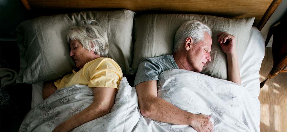 A senior Caucasian couple is sleeping comfortably in bed together.
