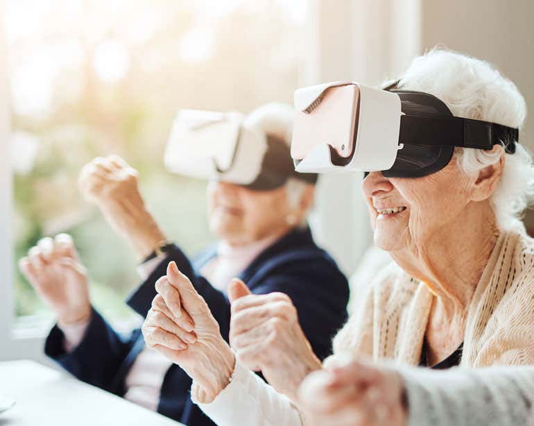 Two senior women are at a senior center, using virtual reality goggles during a group activity.