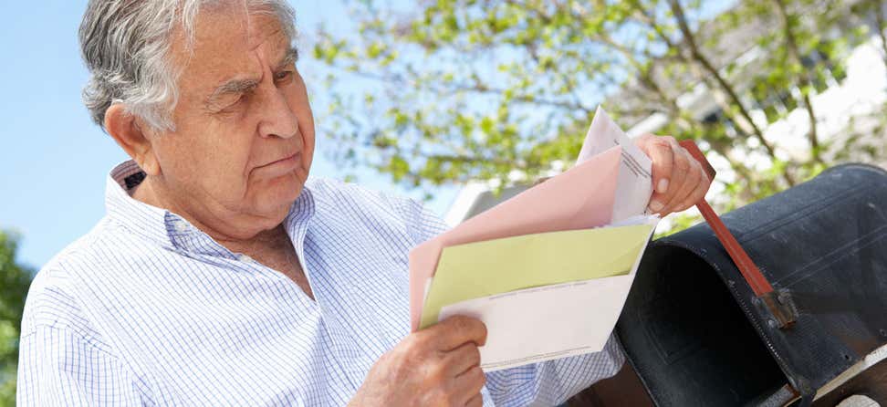 Older Hispanic man getting mail out of his mailbox outside.