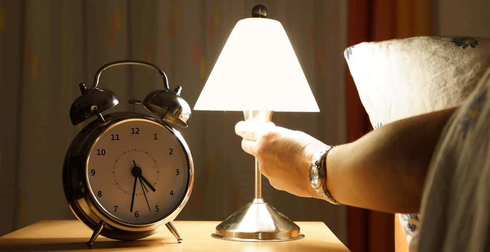 Person reaching to turn off lamp next on bedside table