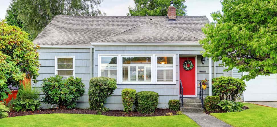A picturesque street view of a cozy bungalow home with blue paint and a red door.