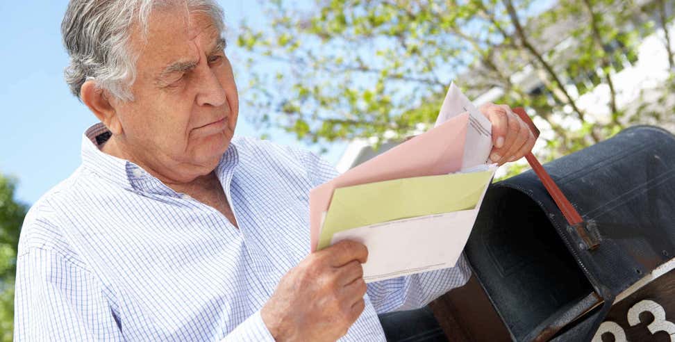 Older man checking letter at mailbox.