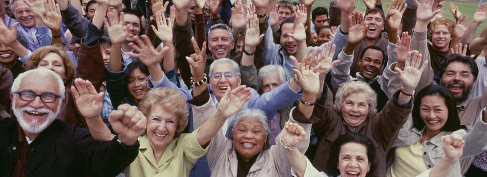 A large group of older adults, all multi-ethnic, have their arms raised and are cheering with joy.