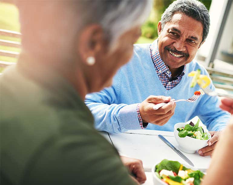 A senior Black man is enjoying a salad with his wife at lunchtime.