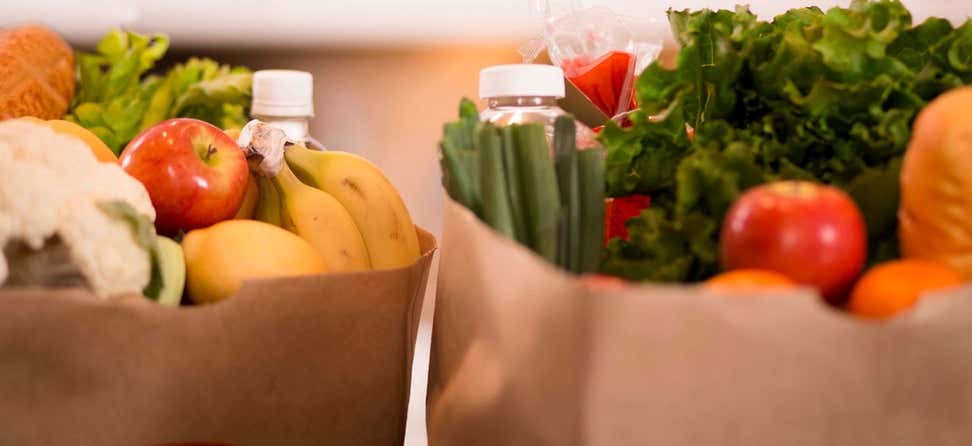 A closeup shot of two paper bags of fresh produce and other groceries atop a counter.