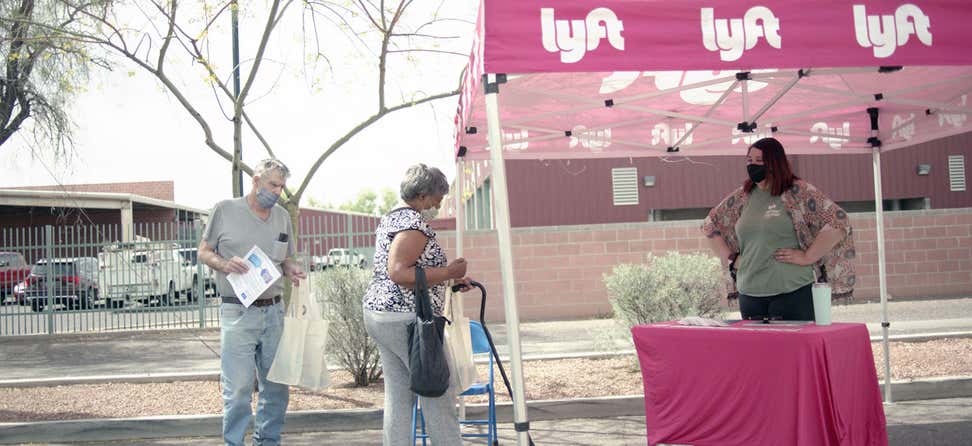 A senior Black woman gets dropped off at a Lyft tent during a COVID-19 vaccine event in Arizona.