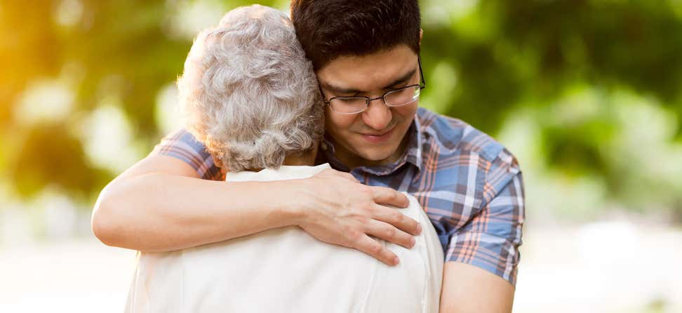 Younger male wearing glasses is hugging a senior woman.