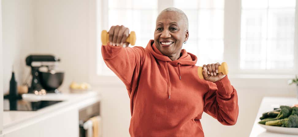 A senior Black woman is exercising with dumbbells at home.